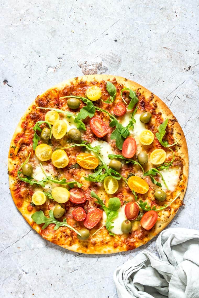 cooked pizza with olives, tomatoes and basil toppings