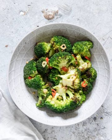 Grilled Broccoli in a bowl seasoned with garlic and chilli and a grey cloth on the side