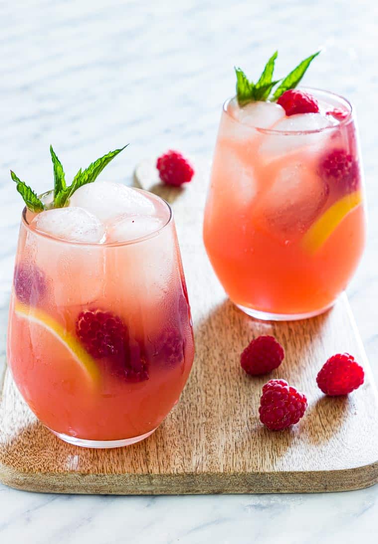 2 glasses of pink vodka lemonade on a table with mint and raspberries