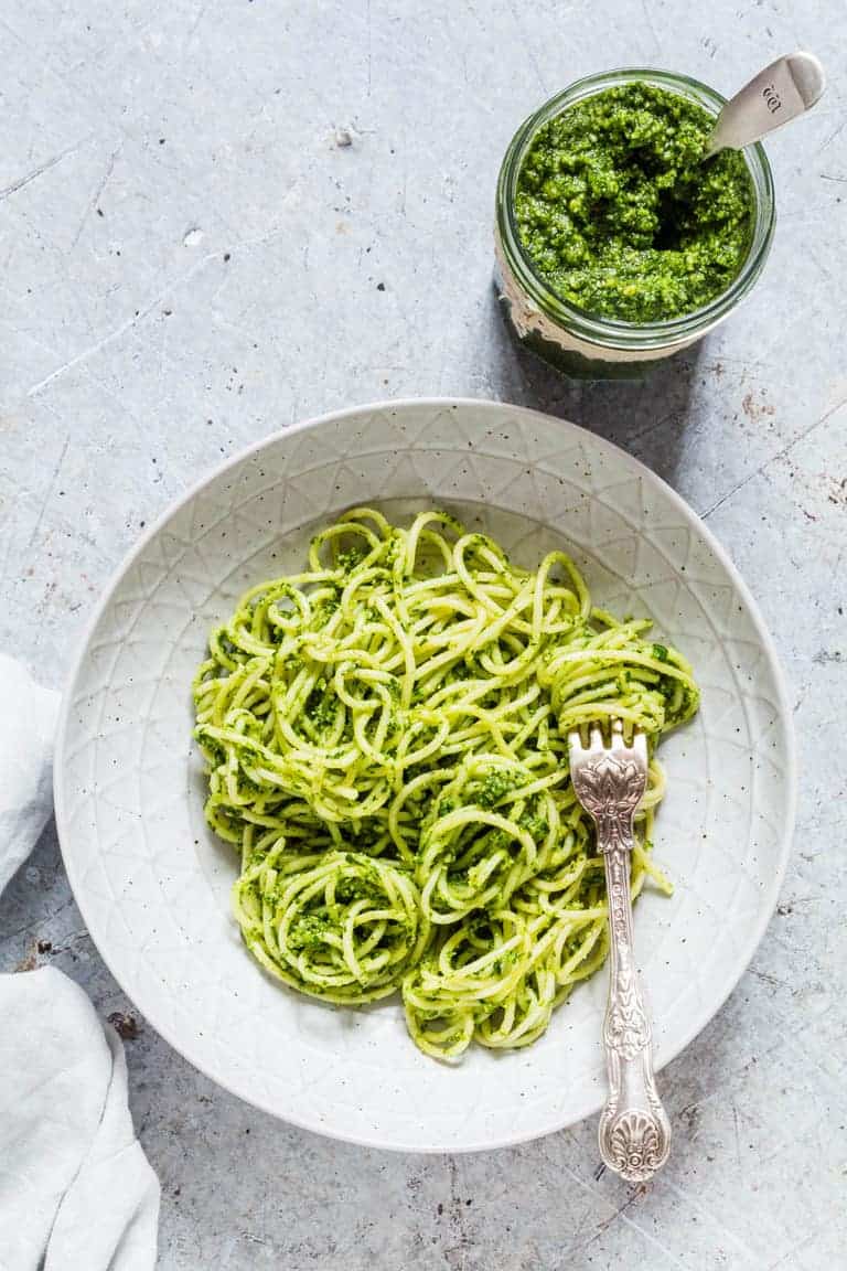 basil pesto in a glass jar next to a dish containing one serving of pasta and pesto