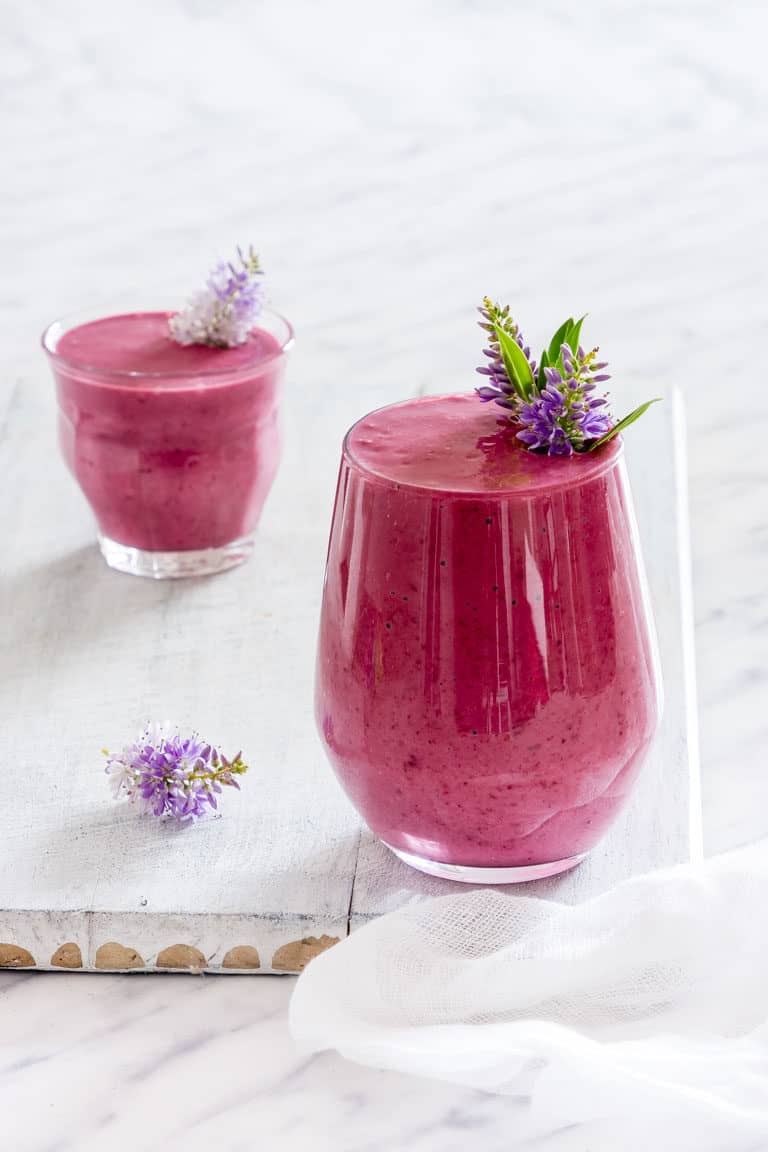2 glasses of blackberry smoothie on a white tabel