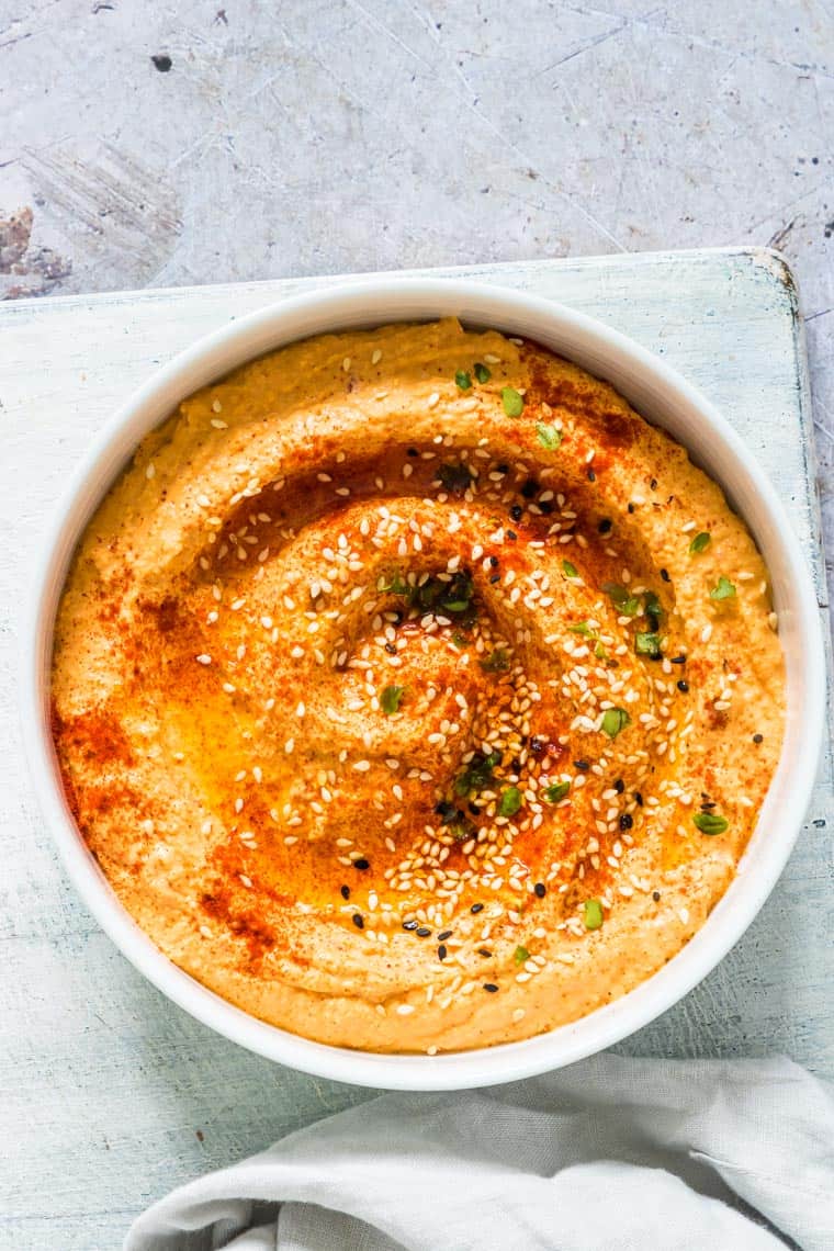 close up of creamy pumpkin hummus on a table topped with sesame seeds
