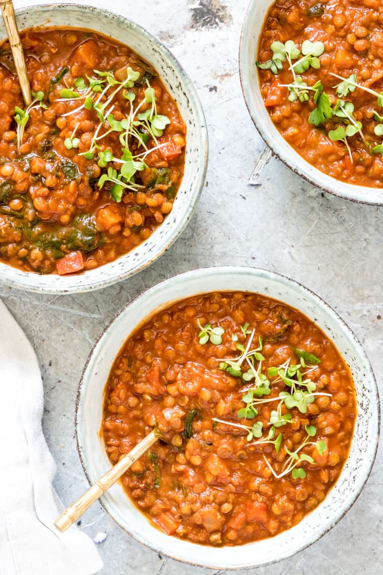 three bowls of vegan lentil curry on a table