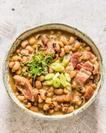 A bowl of Hoppin’ John soup garnished with bacon, spring onion and cress