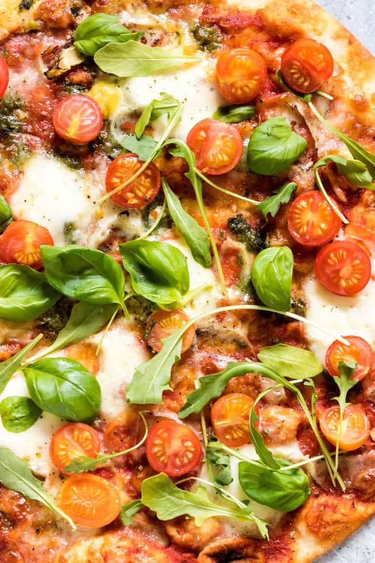 closeup of cooked italian pizza dough recipe with toppings like basil and tomatoes