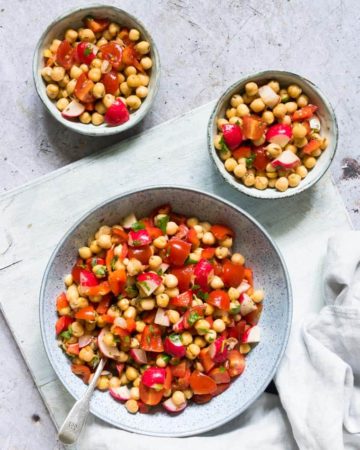 a serving bowl filled with instant pot chickpeas salad placed on a cloth napkin with two individual portions in smaller bowls