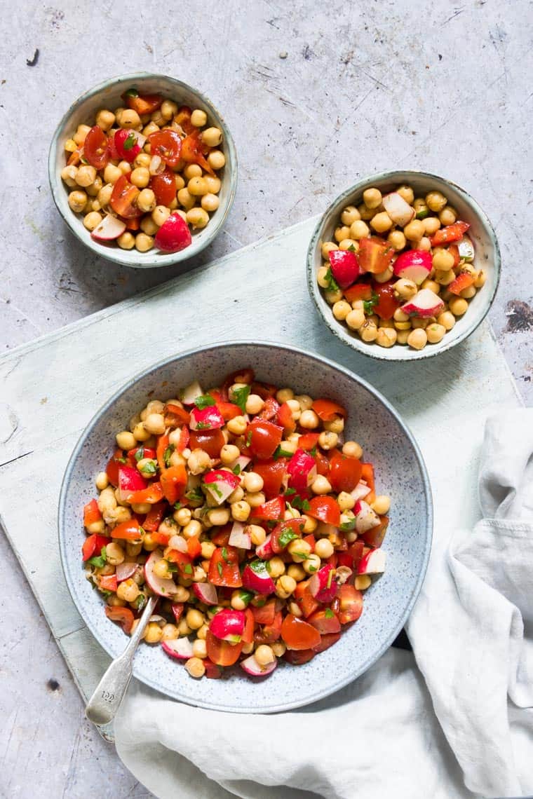 a serving bowl filled with instant pot chickpeas salad placed on a cloth napkin with two individual portions in smaller bowls