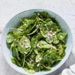 easy spinach salad recipe in a bowl with onion and sesame seeds