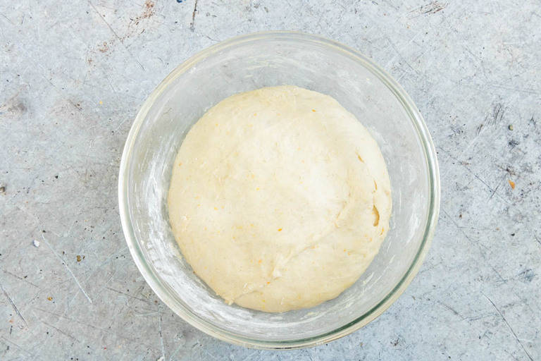 overhead view of risen orange cardamom buns dough in a clear bowl