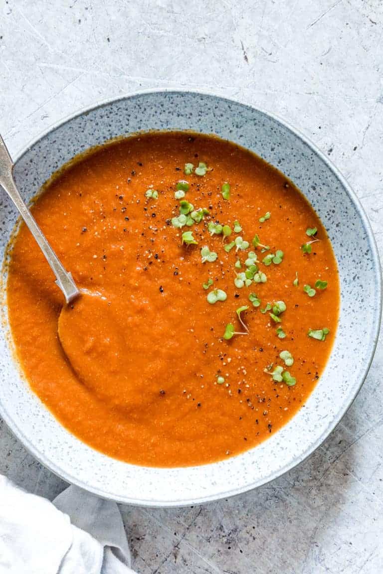 a bowl of vegan tomato soup on a table with a spoon