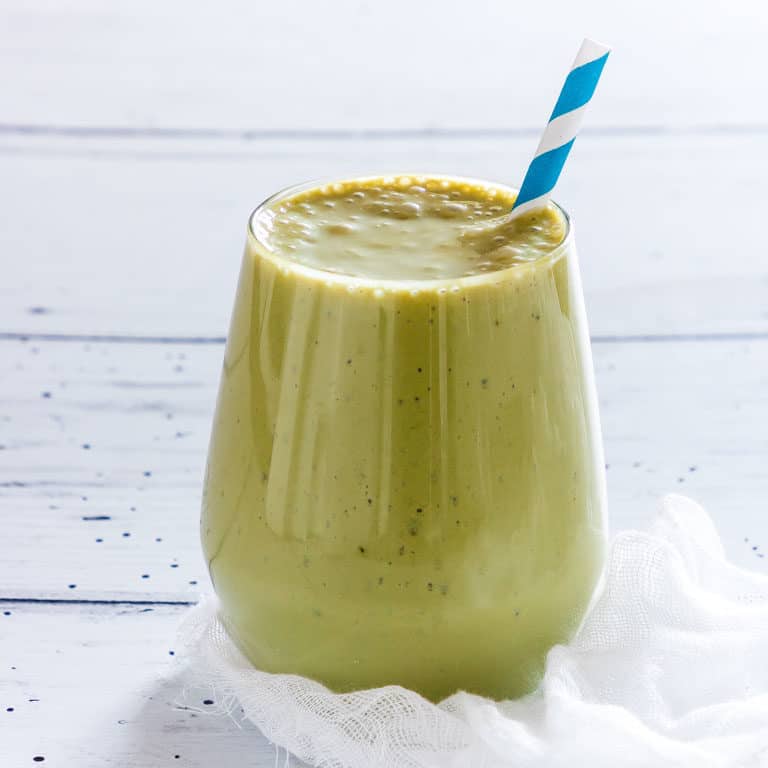 Close up of a Matcha Smoothie (green Tea Smoothie) in a glass on a white table with a blue striped straw