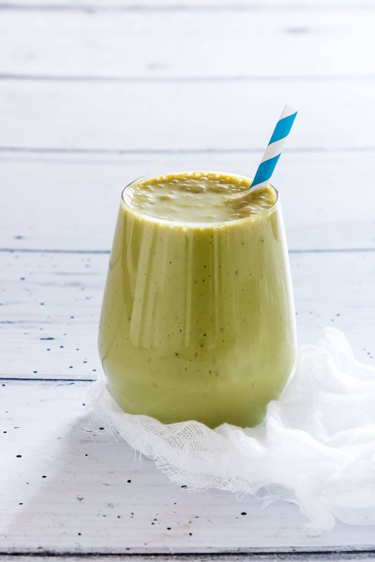 Matcha Smoothie (green Tea Smoothie) in a glass on a white table with a blue striped straw