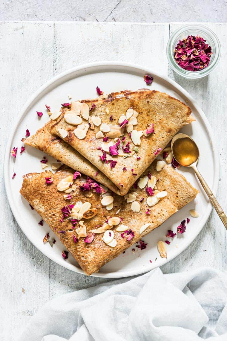 two plantain pancakes topped with sliced almonds, pomegranate seeds and served with a side of syrup