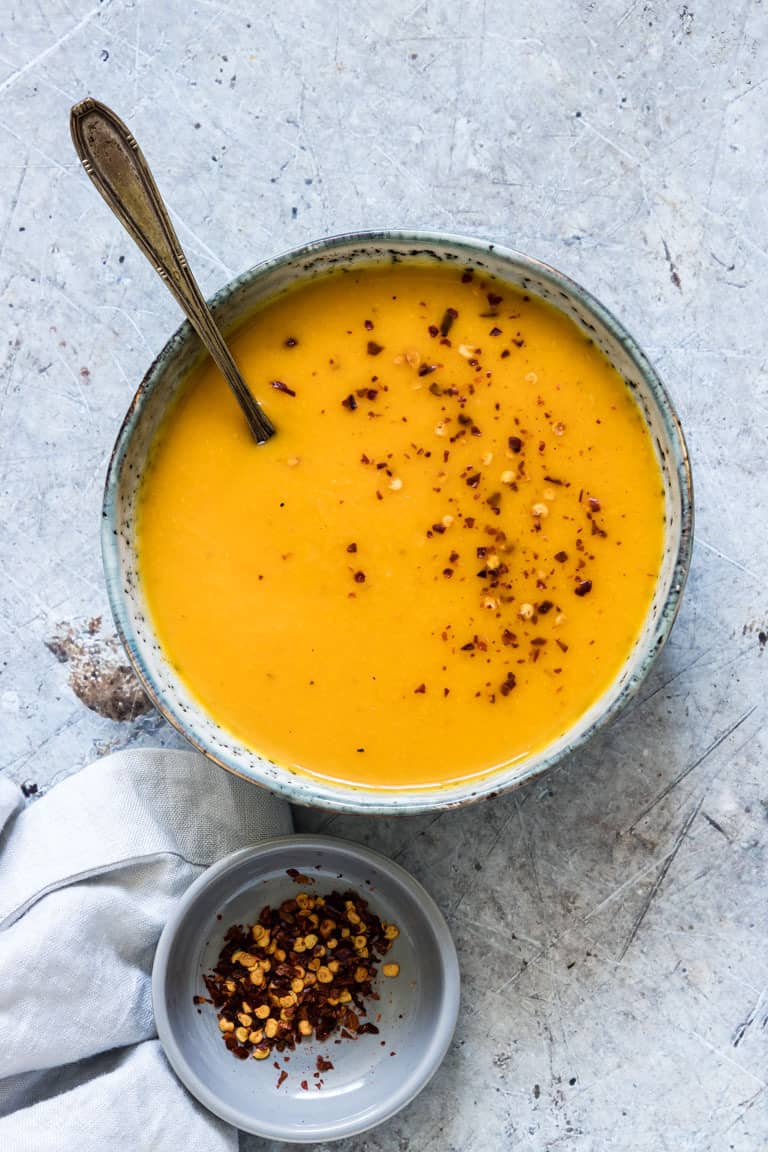 bowl of peanut butter and kabocha squash soup on a table with a spoon in it