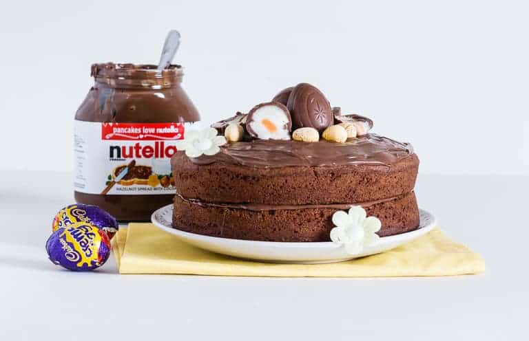 Easy Nutella Cake topped with nutella frosting and some cadbury creme eggs, with a jar of nutella at the back 