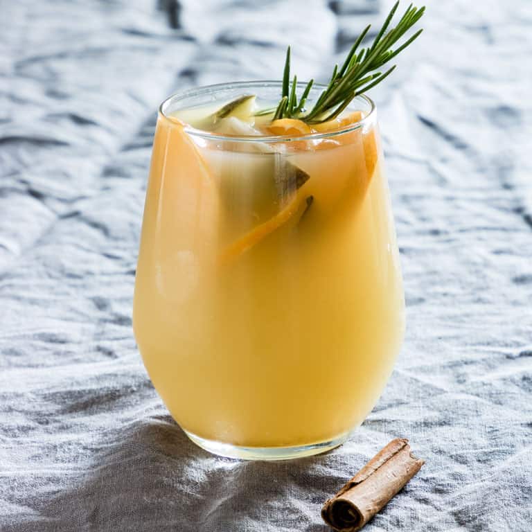 A glass of warm spiced pear juice garnished with fruit and rosemary