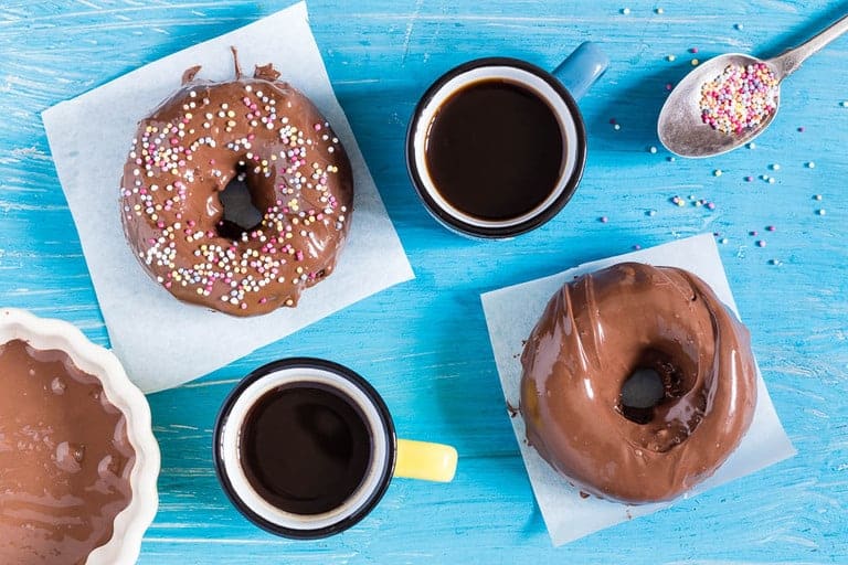 two nutella donut pieces on white napkins next to coffee cups and a spoon with sprinkles