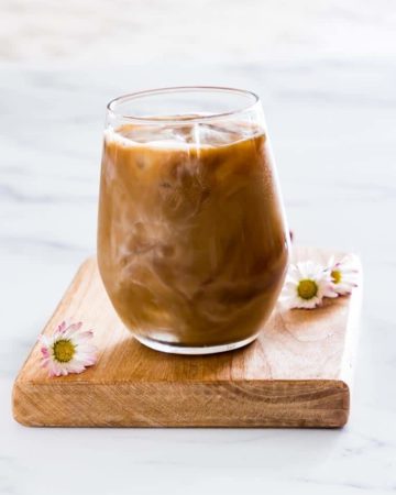 A Glass of Iced Coffee with flowers around it