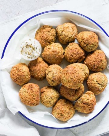 blue rimmed plate filled with cooked air fryer falafel and a cup of tahini yogurt sauce