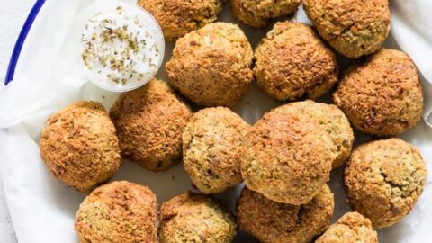 blue rimmed plate filled with cooked air fryer falafel and a cup of tahini yogurt sauce