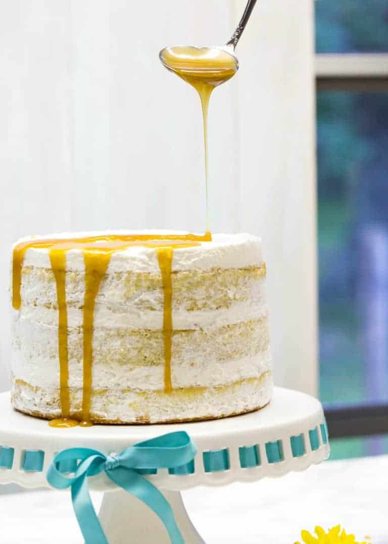 caramel drizzle being drizzled on top of mango cake on cake stand