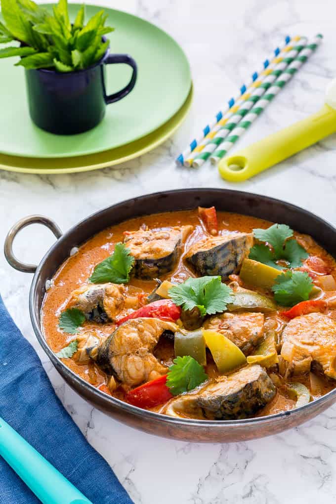 A Pot of Moqueca Baiana (Brazilian Fish Stew) with plates, spoons and straws around it with a blue napkin