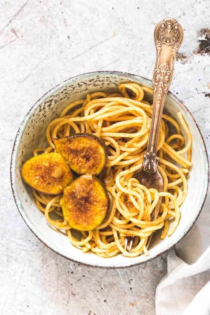 A bowl of saffron sauce pasta with figs with a fork