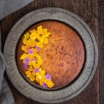 overhead view of cinnamon plantain cake with flowers on the left of the cake