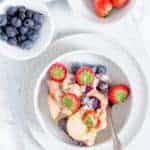 Slow cooker french toast casserole in a white bowl with additional fruits in seperate bowls.
