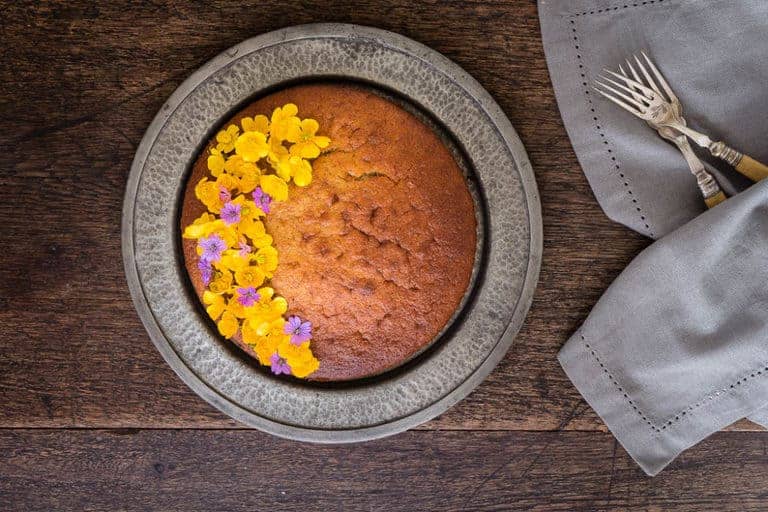 overhead view of cinnamon plantain cake in a decorative dish with yellow flowers