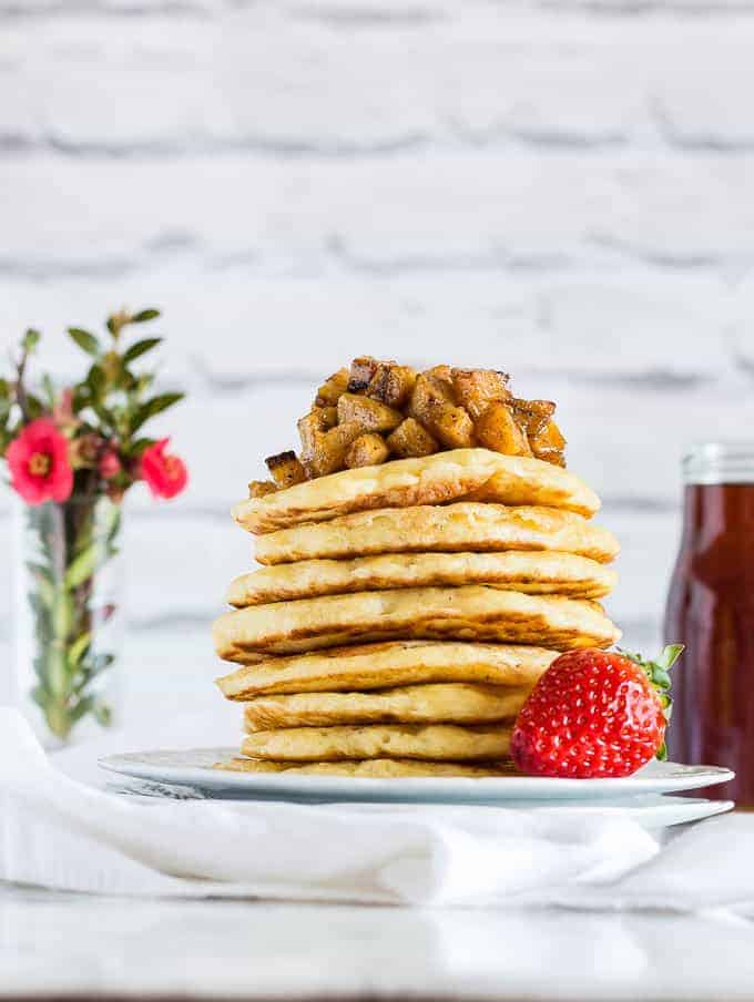 A stack of vegan pancakes (beghrir, baghrir) on a white plate toped with plantain cubes and strawberries