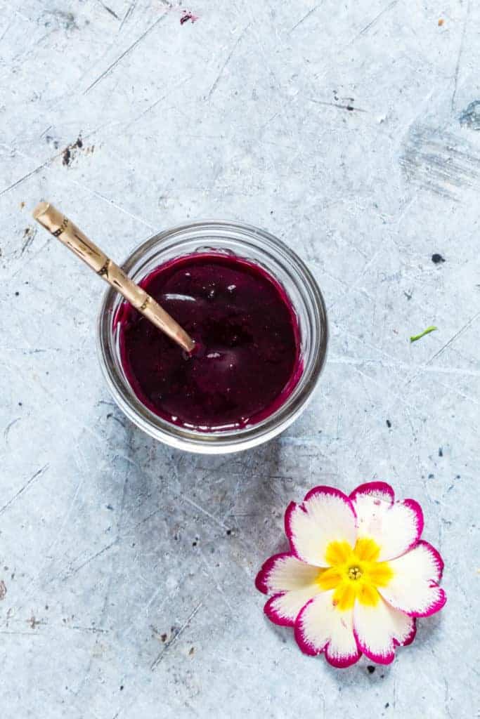 An easy blueberry glaze in a jar with a spoon and a flower