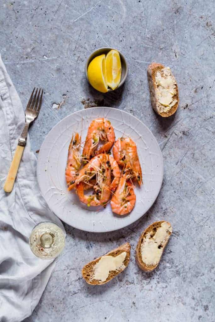  quick garlic butter chilli shrimps on a plate with lemon, buttered bread and wine 