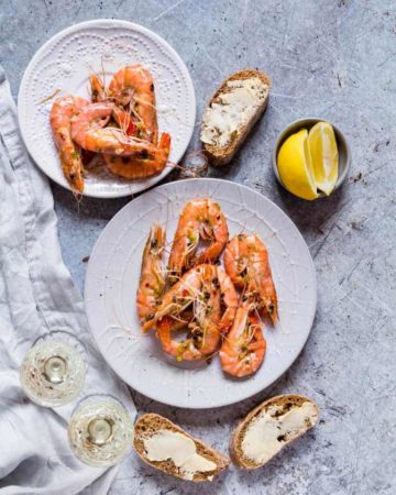 quick garlic butter chilli shrimps on a plate with lemon, buttered bread and wine