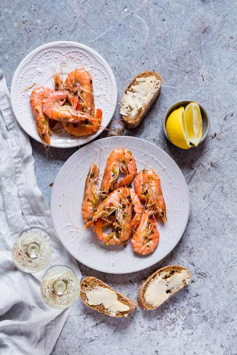 quick garlic butter chilli shrimps on a plate with lemon, buttered bread and wine