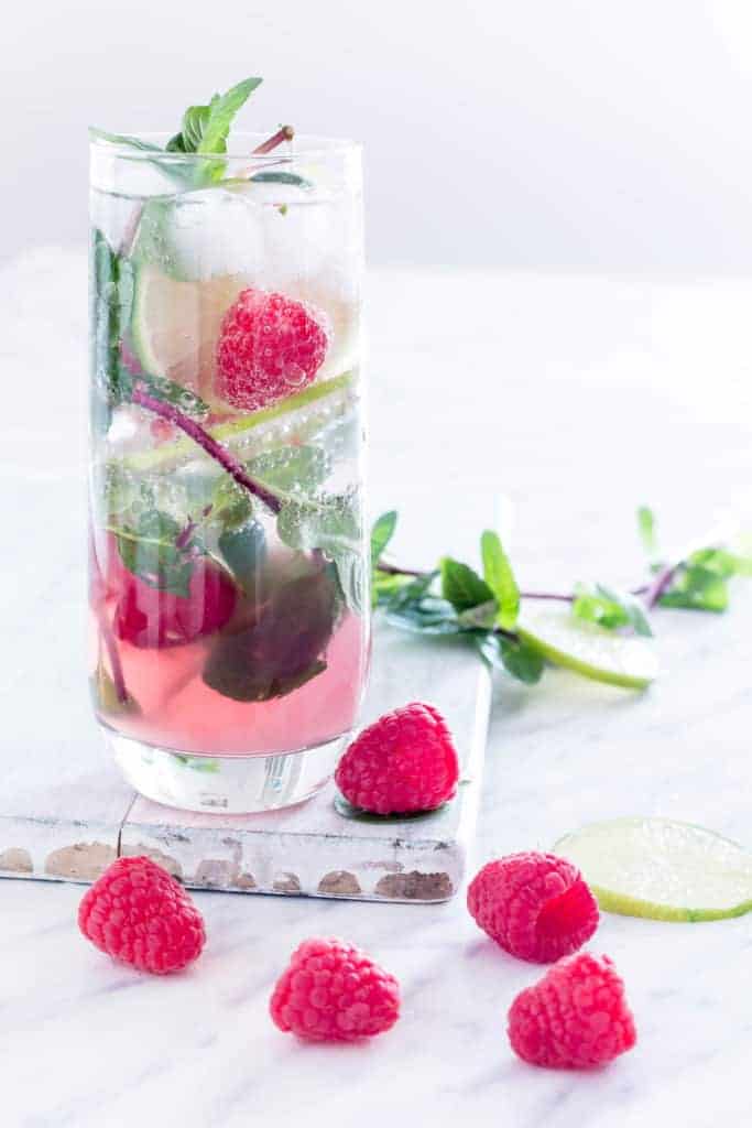 A glass of Raspberry Mojito with raspberries and lime