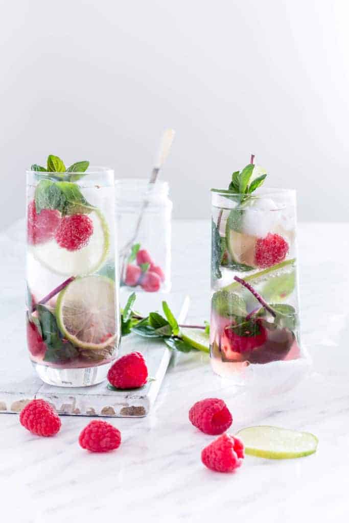 Two glasses of Raspberry Mojito with raspberries, lime and mint around