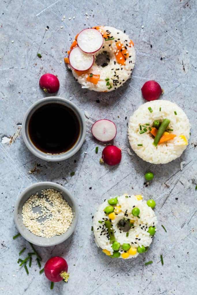 3 Vegetable Sushi Donuts - sushi doughnuts - on a table with some soy sauce and sesame seeds