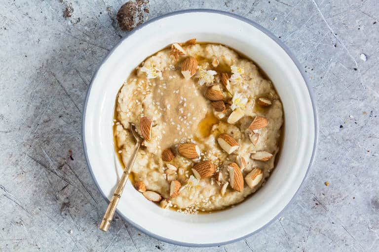 view of white bowl with blue rim containing tahini porridge with peanut butter on top
