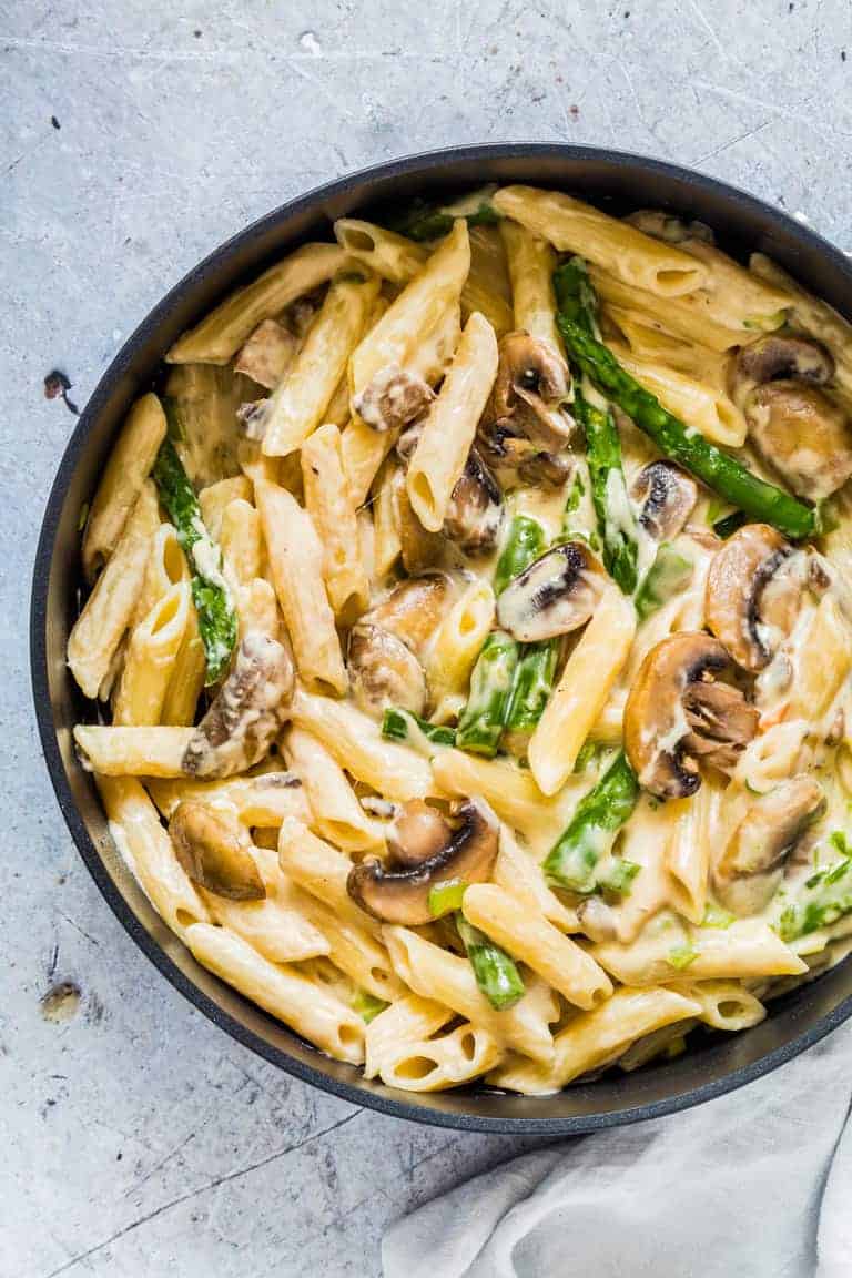 overhead view of cooked mushroom asparagus pasta in a black skillet next to a grey towel