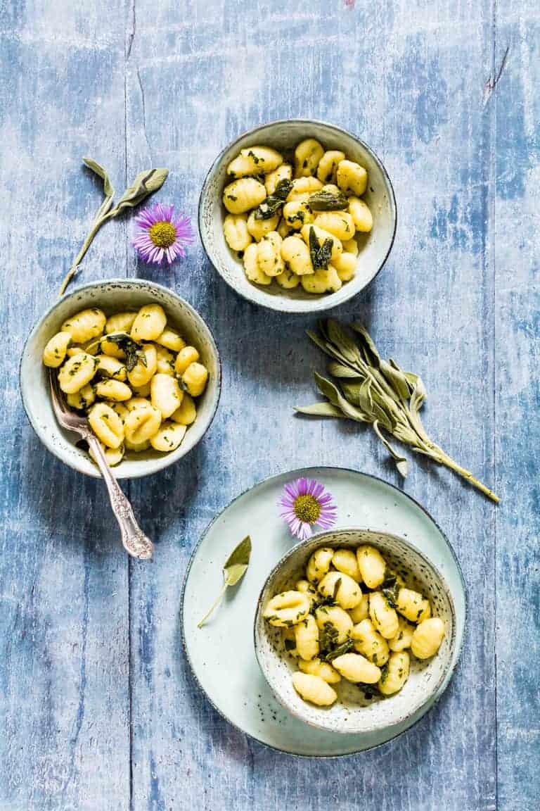 3 bowls of sage and brown butter gnocchi sauce over gnocchi on a table with extra sage