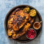 grilled whole chicken in a tray with limes and pomegranate