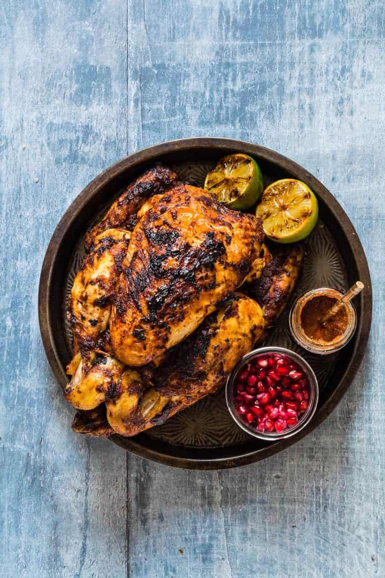 grilled whole chicken in a tray with limes and pomegranate