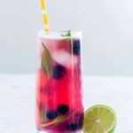 a glass of blueberry mojito with some lime and blueberries