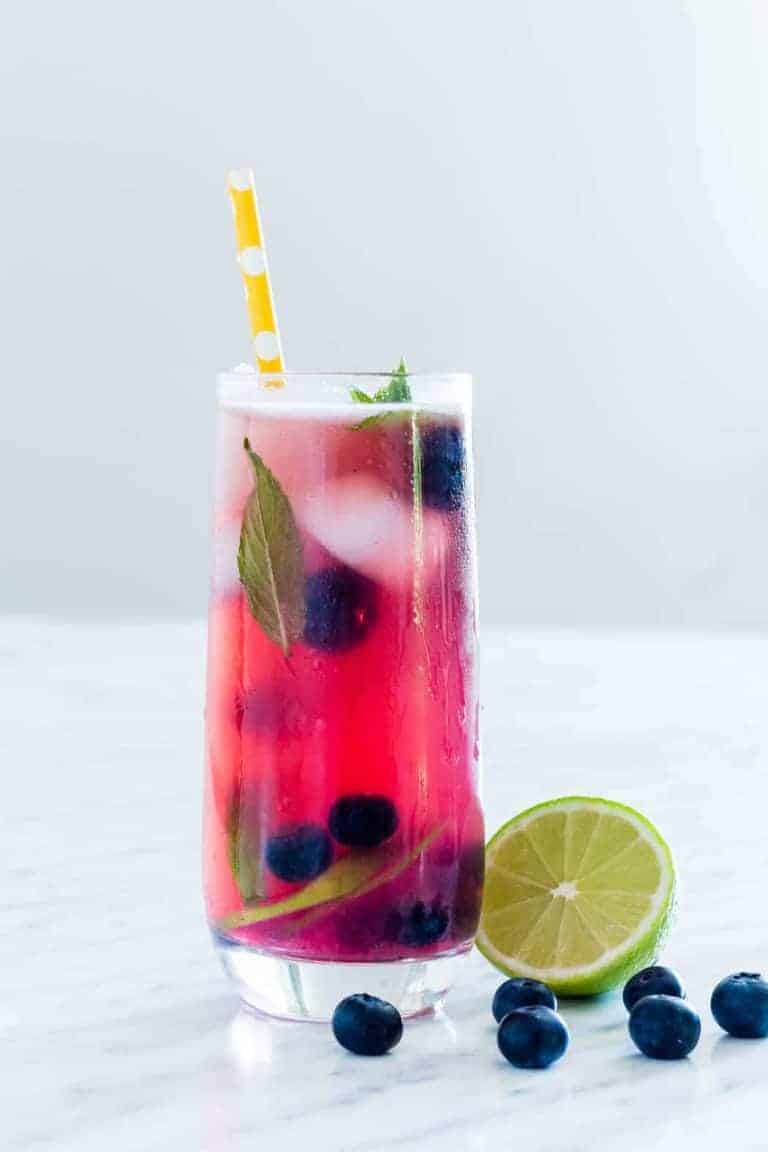 a glass of blueberry mojito with some lime and blueberries