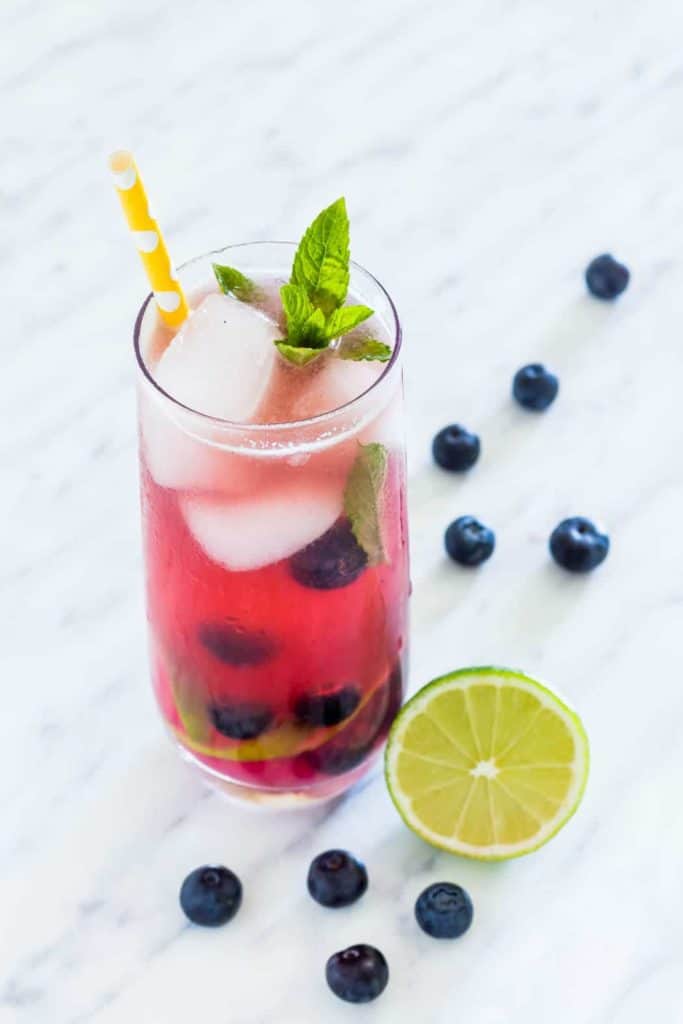 a glass of blueberry mojito with some lime and blueberries and a straw