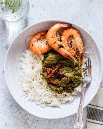 Overhead shot of a bowl of palava sauce - cooked cassava leaves with rice with prawns and chilli with a glass of water next to it