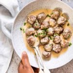 A hand holding a bowl of Swedish meatball in a creamy sauce