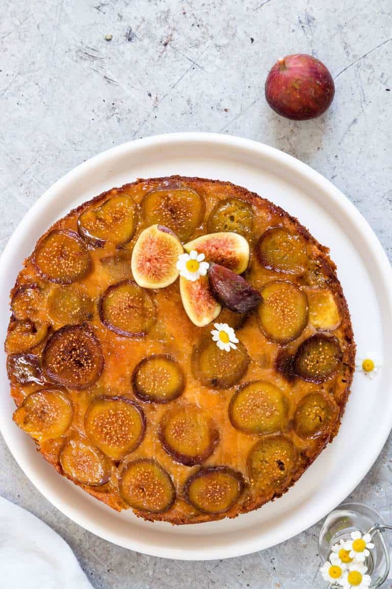 A plate Upside Down Fresh Fig Cake on aplate with flowers and a fig