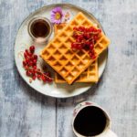 overhead shot of honey waffles on a plate with blue rim next to a cup of coffee